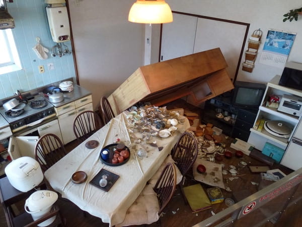 背の高い家具が倒れ、中の食器が飛び出して割れている地震の後の写真